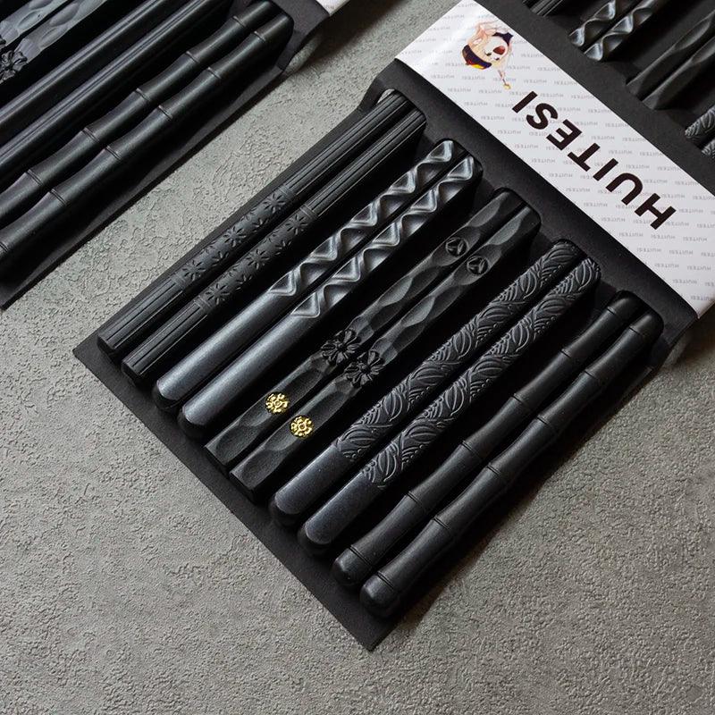 Schwarze Essstäbchen mit verschiedenen Mustern, stilvolles Küchenaccessoire auf grauer Oberfläche