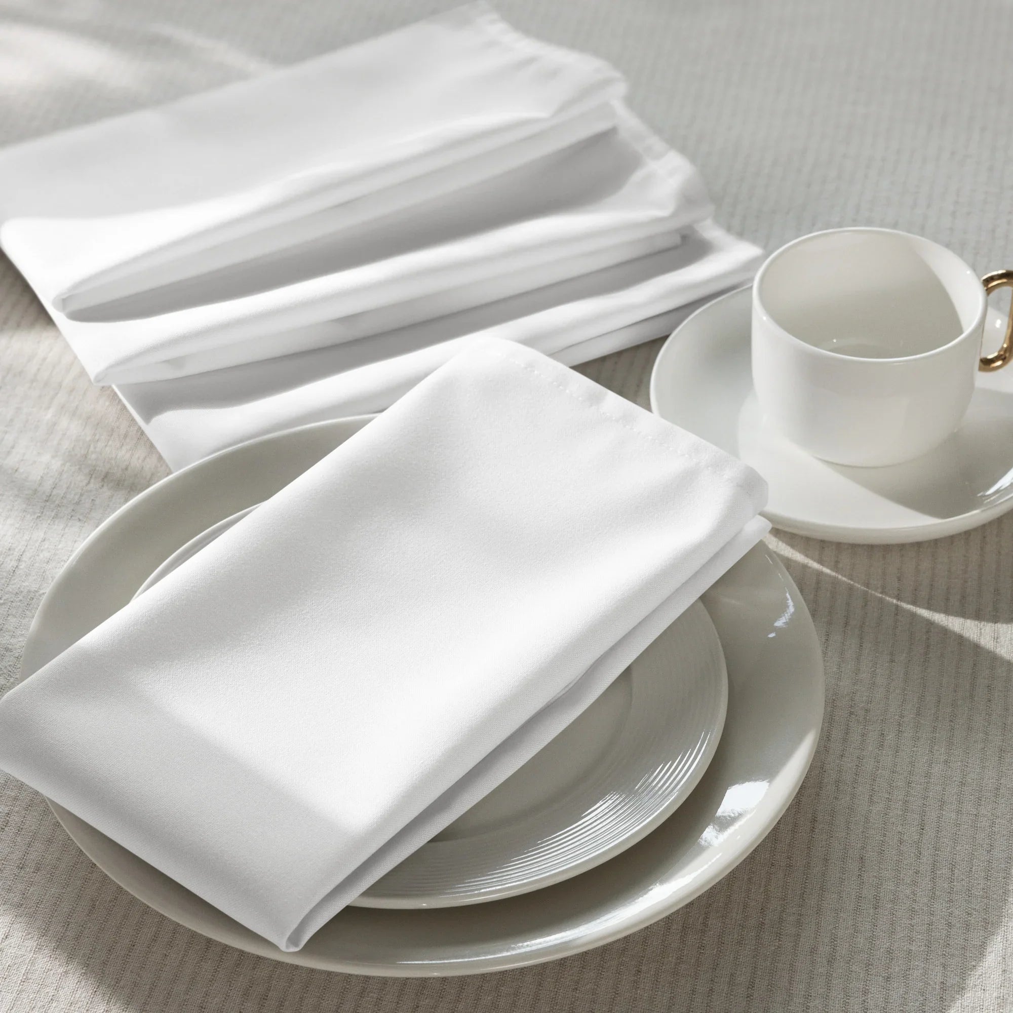 Weiße Stoffservietten Set, stilvoll arrangiert auf Porzellangeschirr und Tasse, Küchenaccessoire