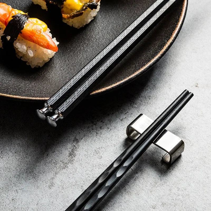 Schwarze Essstäbchen aus Metall mit Sushi auf Keramikteller, stilvolle Küchenutensilien
