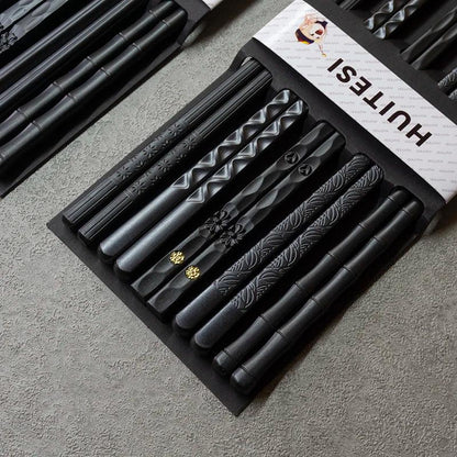 Schwarze Essstäbchen mit verschiedenen Mustern, stilvolles Küchenaccessoire auf grauer Oberfläche