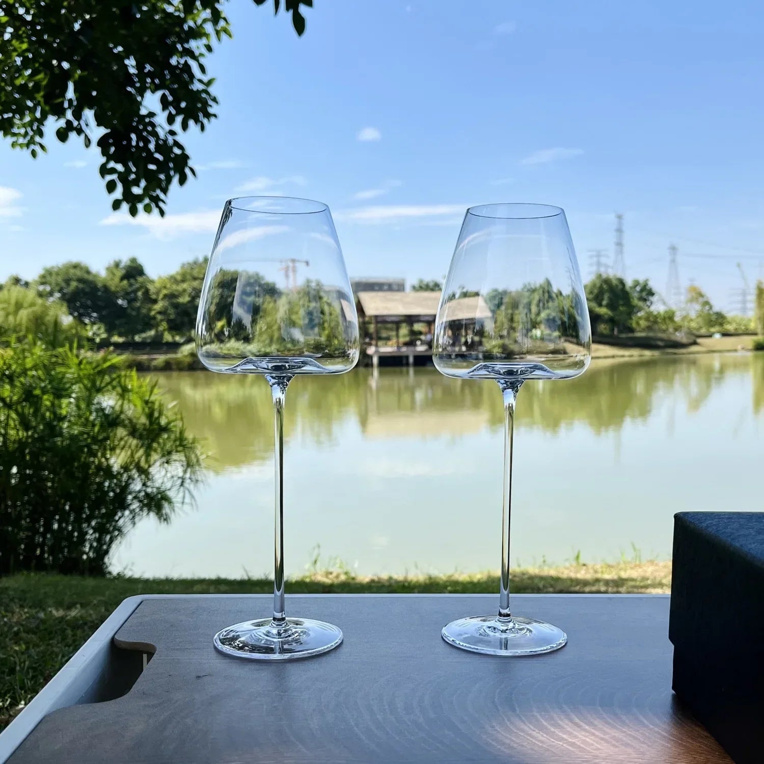 Zwei elegante Weingläser aus Glas auf Tisch im Freien mit Blick auf See und Natur