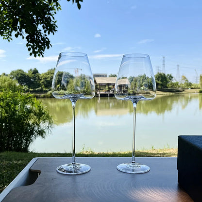 Zwei elegante Weingläser aus Glas auf Tisch im Freien mit Blick auf See und Natur