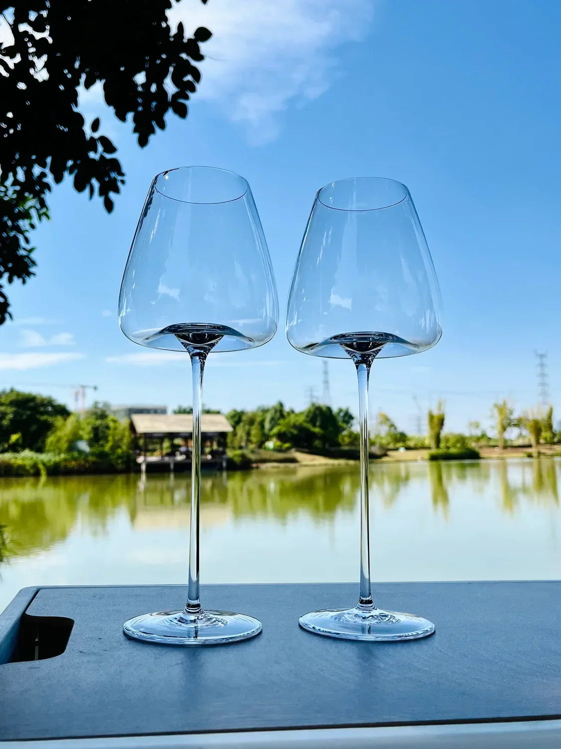 Zwei elegante Weingläser auf einem Tisch am See, stilvolle Küchenaccessoires im Freien