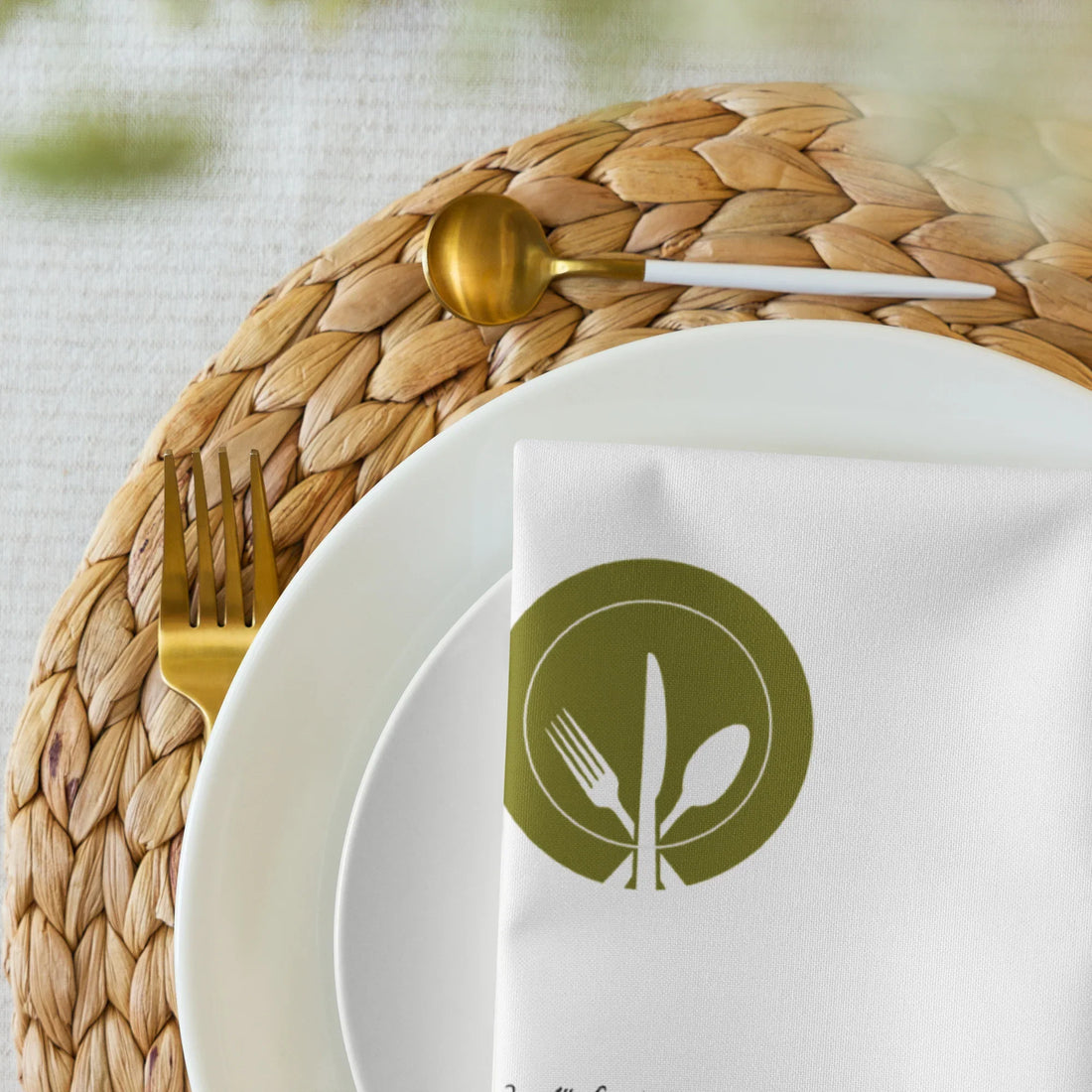 Elegante weiße Serviette mit Besteckmotiv auf geflochtenem Platzset, goldenem Besteck und weißem Teller, stilvolle Küchendeko von Kochschein